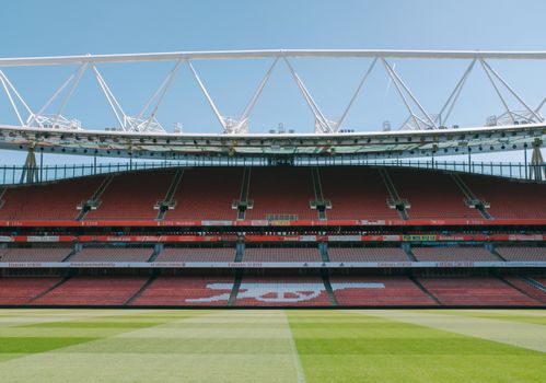 Telefoonscherm met stand eredivisie naast voetbalveld en supporters op de tribune